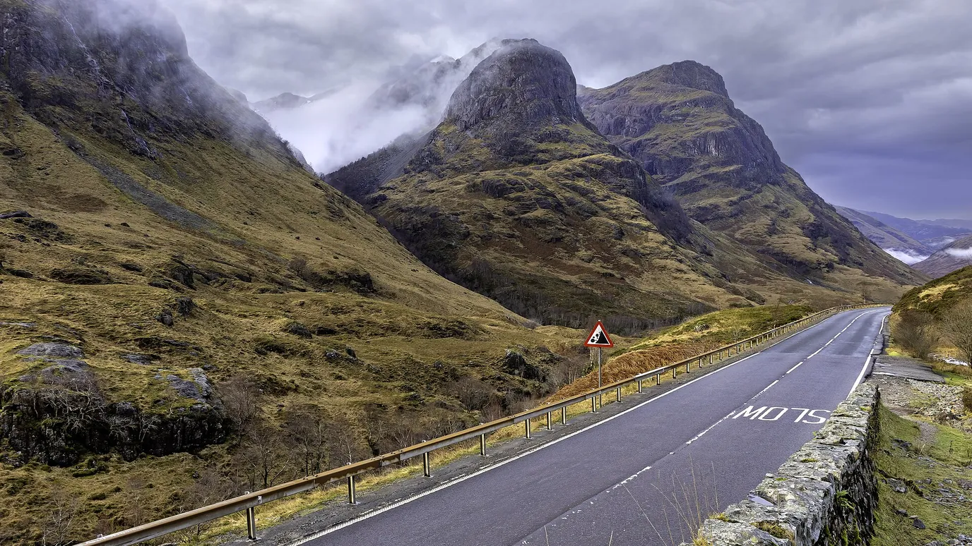 The Three Sisters, steep green mountains above the road through Glencoe, under low cloud.