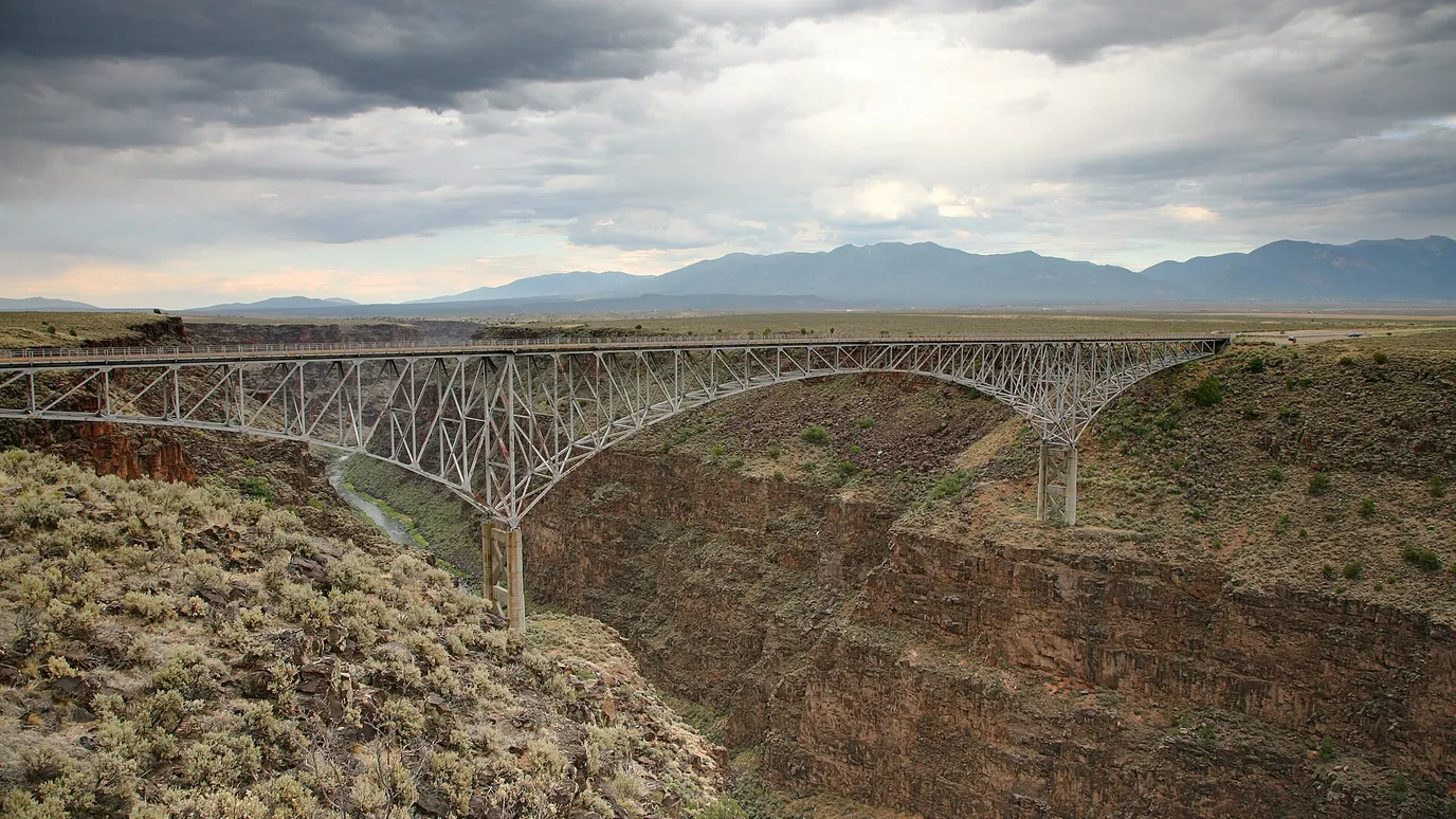 The Rio Grande Gorge Bridge arching over a deep canyon under a cloudy sky.